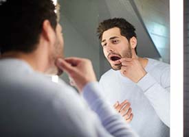 man looking at his tooth in a mirror